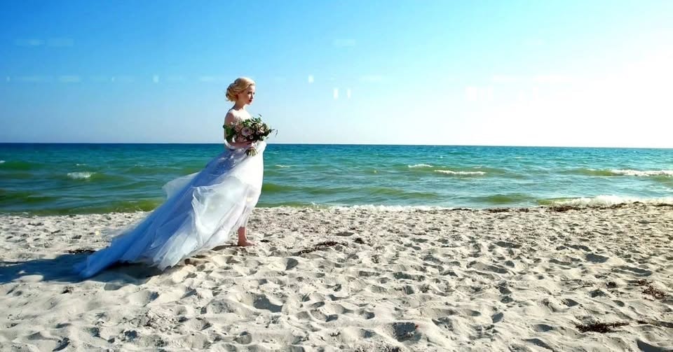 Bride in white gown with bouquet by the ocean